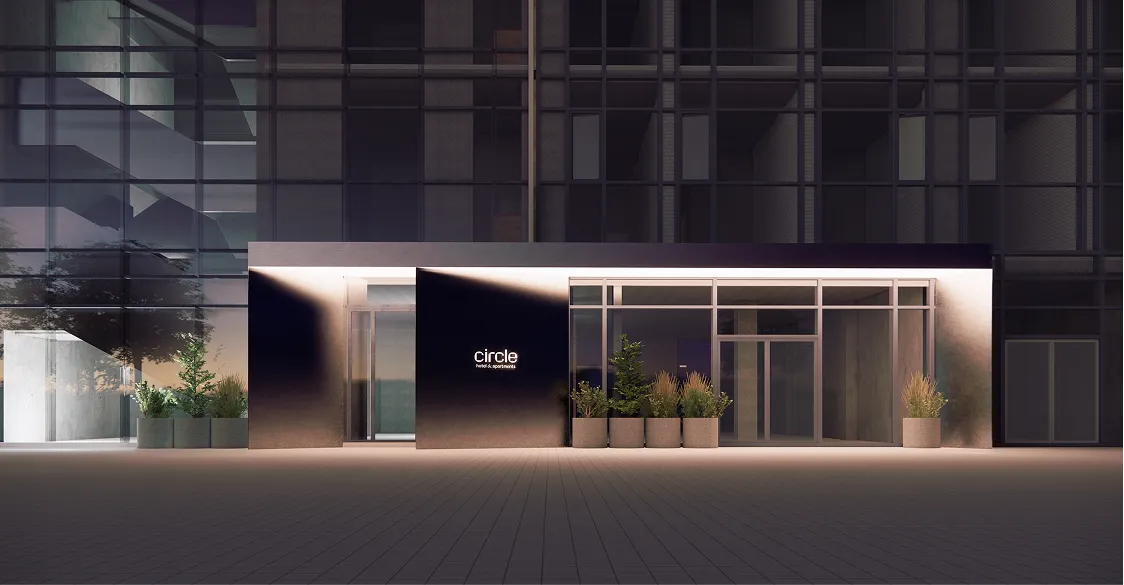 Фасад сучасної будівлі з логотипом Circle (hotel & apartments), великими прозорими вікнами, металевим каркасом, рослинами у горщиках на терасі та вечірнім освітленням.