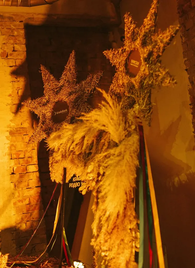 Декор із солом’яних різдвяних зірок і сухих трав на тлі цегляної стіни в теплому жовтому освітленні.