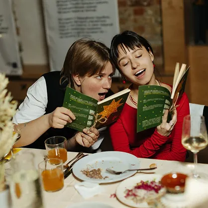 Фотографія двох дівчат з книгами які сидять за святковим столом.